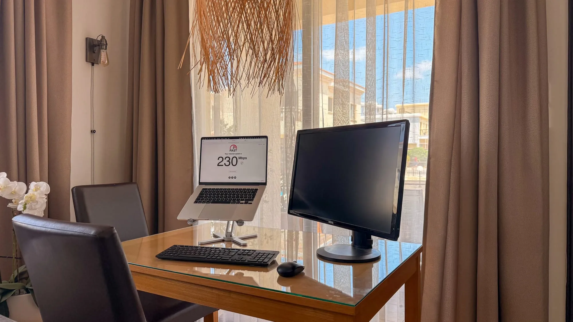 The desk by the window, with a laptop on a stand, external monitor, and a speed test showing 230 Mbps