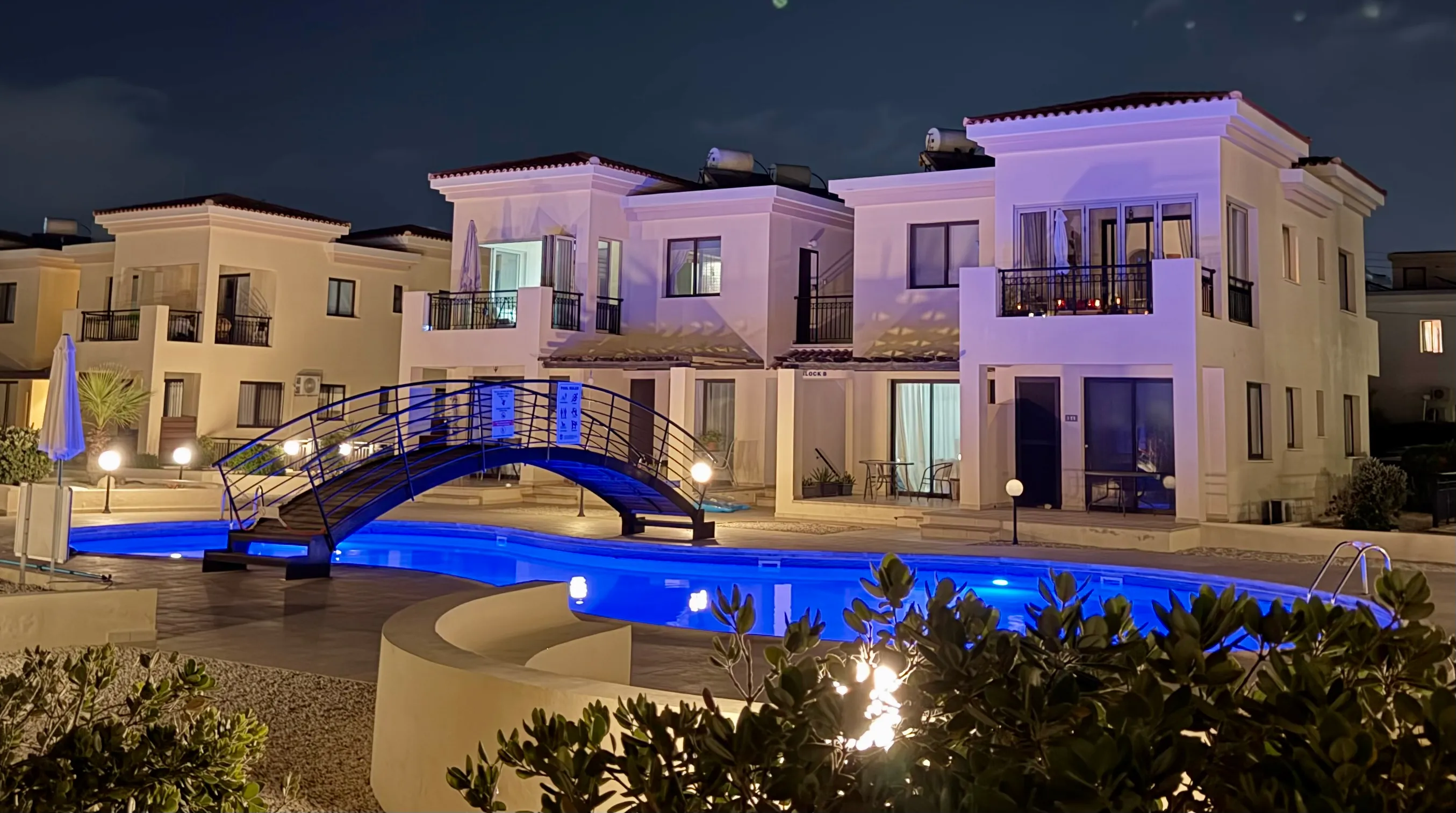 The shared pool at night, lit blue beneath the bridge and the complex lights