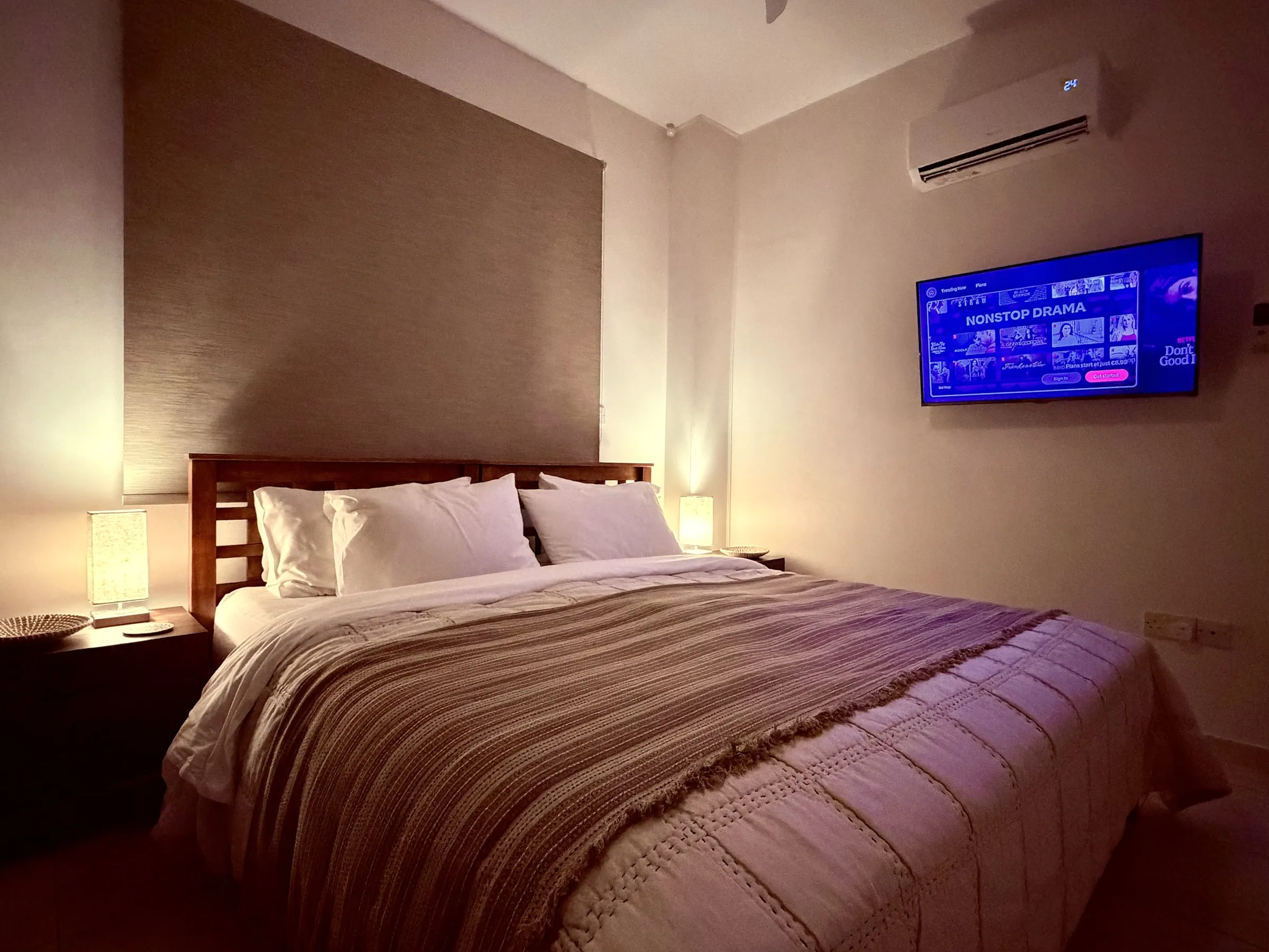 The bedroom TV above the foot of the bed, lit softly by the bedside lamps